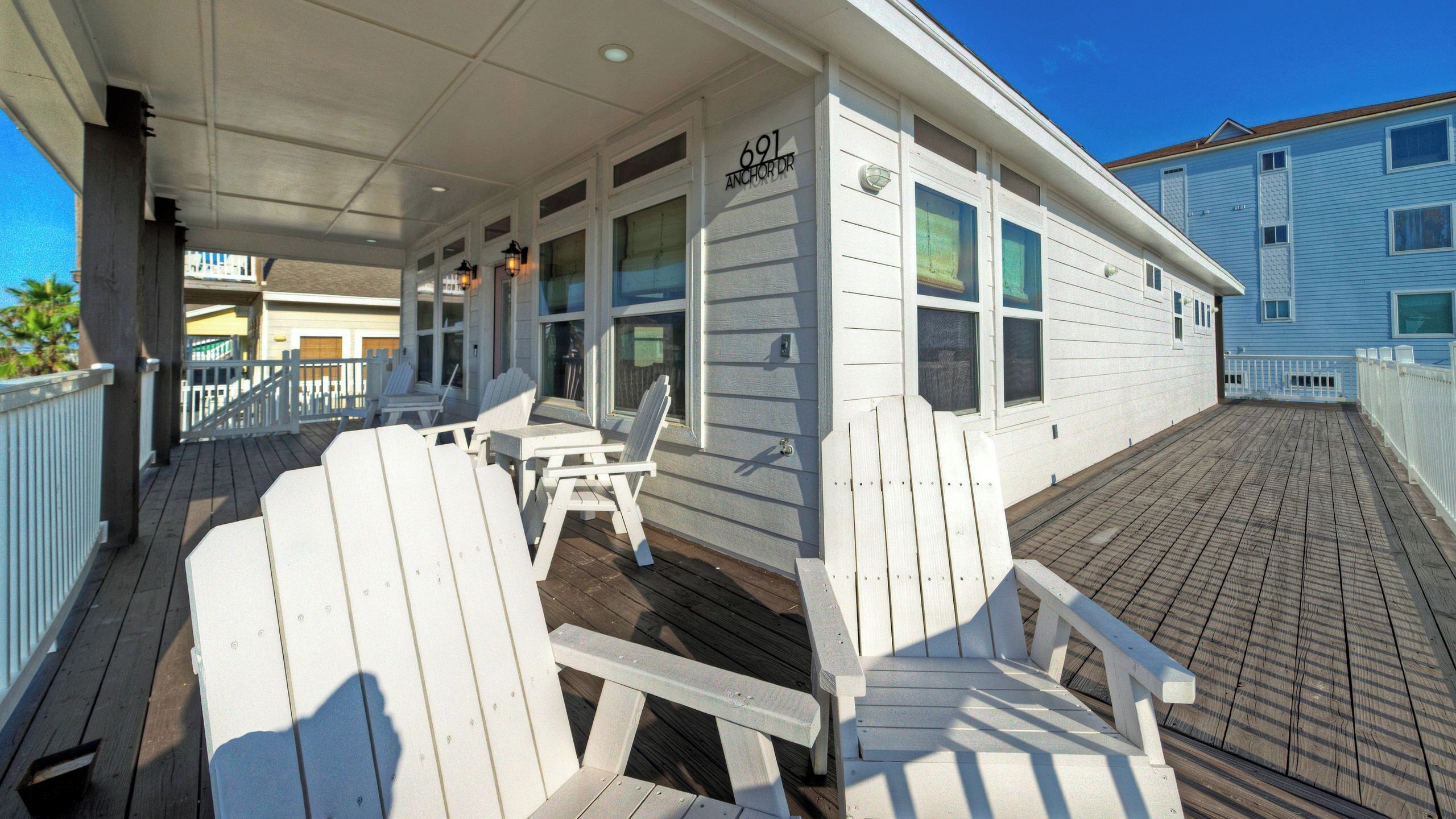 Une terrasse couverte avec des fauteuils Adirondack blancs, une petite table et un bâtiment situé au 691, avenue Anchor.