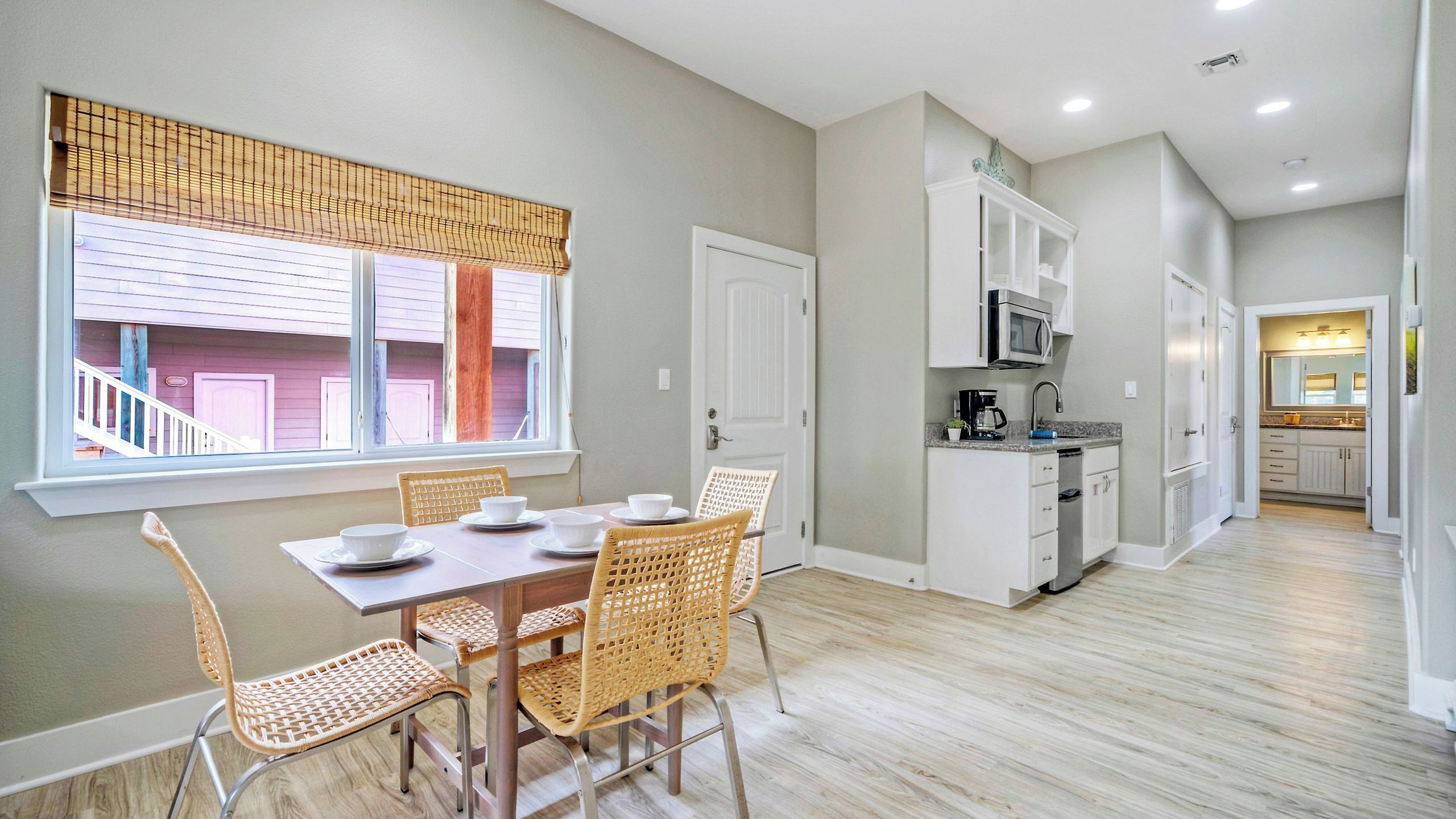 A dining area with a table and chairs, a kitchen with cabinets and appliances, and a view through a window.