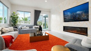 Una sala moderna con chimenea, ventanas amplias y una televisión mostrando un paisaje urbano.