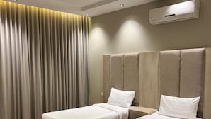 A hotel room with two beds, a large window with curtains, a ceiling light, and an air conditioning unit.