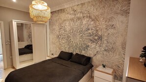 A modern bedroom with a large bed, a bedside table, a nightstand, a hanging light fixture, and a decorative wall mural. - Egypt Hurghada Apartment  (Hurghada)