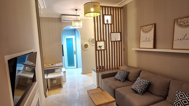A modern living room with a beige sofa, patterned cushions, a small wooden coffee table, and a TV on the left. - Egypt Hurghada Apartment  (Hurghada)