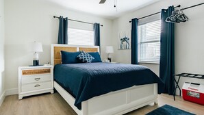 Ein Schlafzimmer mit Bett, Nachttischen, Deckenventilator, einem Fenster mit Vorhängen und einem Playmate Wäschekorb.