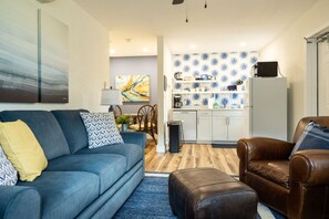 A modern living room with a sofa, a coffee table, and a leather armchair. There is a kitchen area with white cabinets and a patterned backsplash. - New & Blue - 2 blocks to the beach (Pompano Beach)