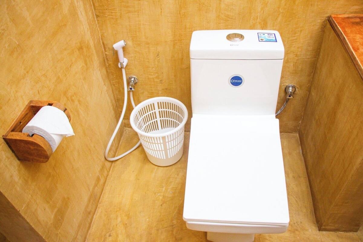 A toilet with a white tank and a control panel, a white plastic basket, and a wooden box with a roll of toilet paper.
