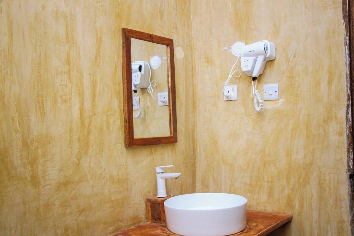 A bathroom with a wooden vanity, a round sink, a mirror, and two hair dryers mounted on the wall.