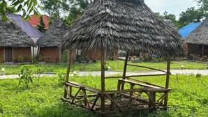 A rustic thatched-roof structure surrounded by lush greenery and traditional buildings with red roofs. - zanzigo (Nungwi)