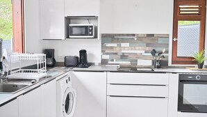 Ett modernt kök med vita skåp, tvättmaskin, mikrovågsugn och kaffebryggare.