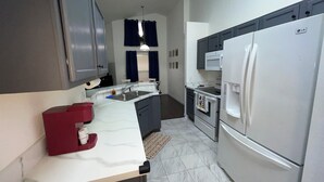 Una cocina moderna con armarios grises, encimera blanca, pileta de acero inoxidable, microondas, estufa y refrigerador blanco.