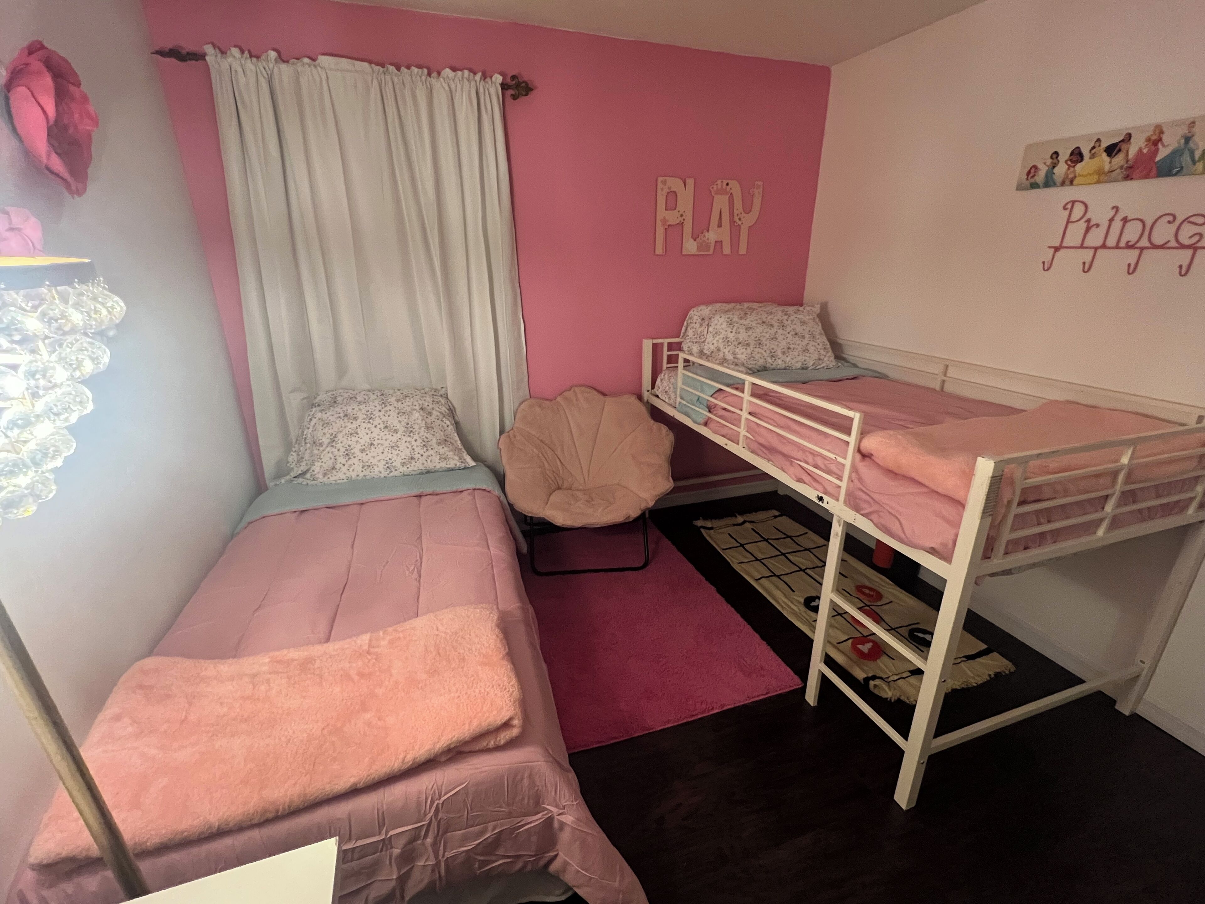 A bedroom with two single beds, a bunk bed, a pink wall, a 'PLAY' sign, and a 'Princess' sign.