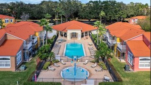 Un resort con piscina central, varias edificaciones para huéspedes con techos rojos y un área ajardinada con palmeras.