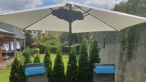 Zwei Liegestühle mit blauen Kissen unter einem großen Sonnenschirm in einem grünen Garten.