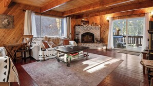 Una sala de estar acogedora con chimenea, techo de madera y un ventanal grande.