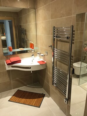 A modern bathroom with a curved sink, a glass shower enclosure, and a wooden bath mat. - Appart One Fréjus (Fréjus)