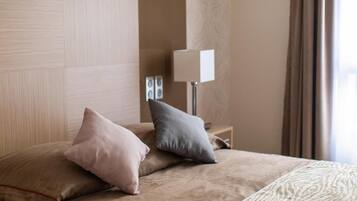 Habitación de hotel con cama, almohadas, mesita de noche, lámpara y ventana con cortinas.
