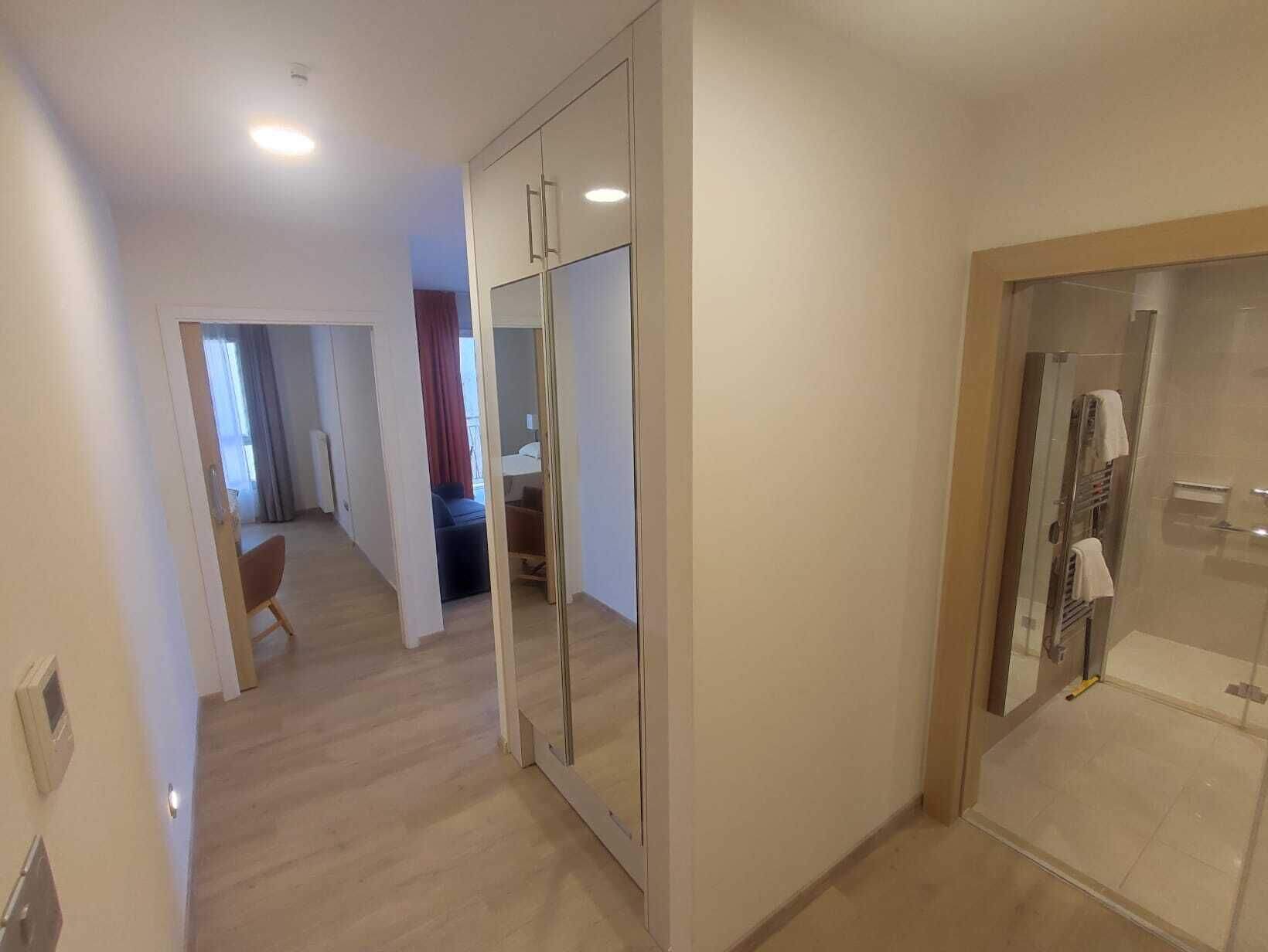 Un couloir avec un placard aux portes miroir, un espace douche et un coin salon comprenant une chaise et une petite table.