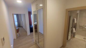 Un couloir avec un placard aux portes miroir, un espace douche et un coin salon comprenant une chaise et une petite table.