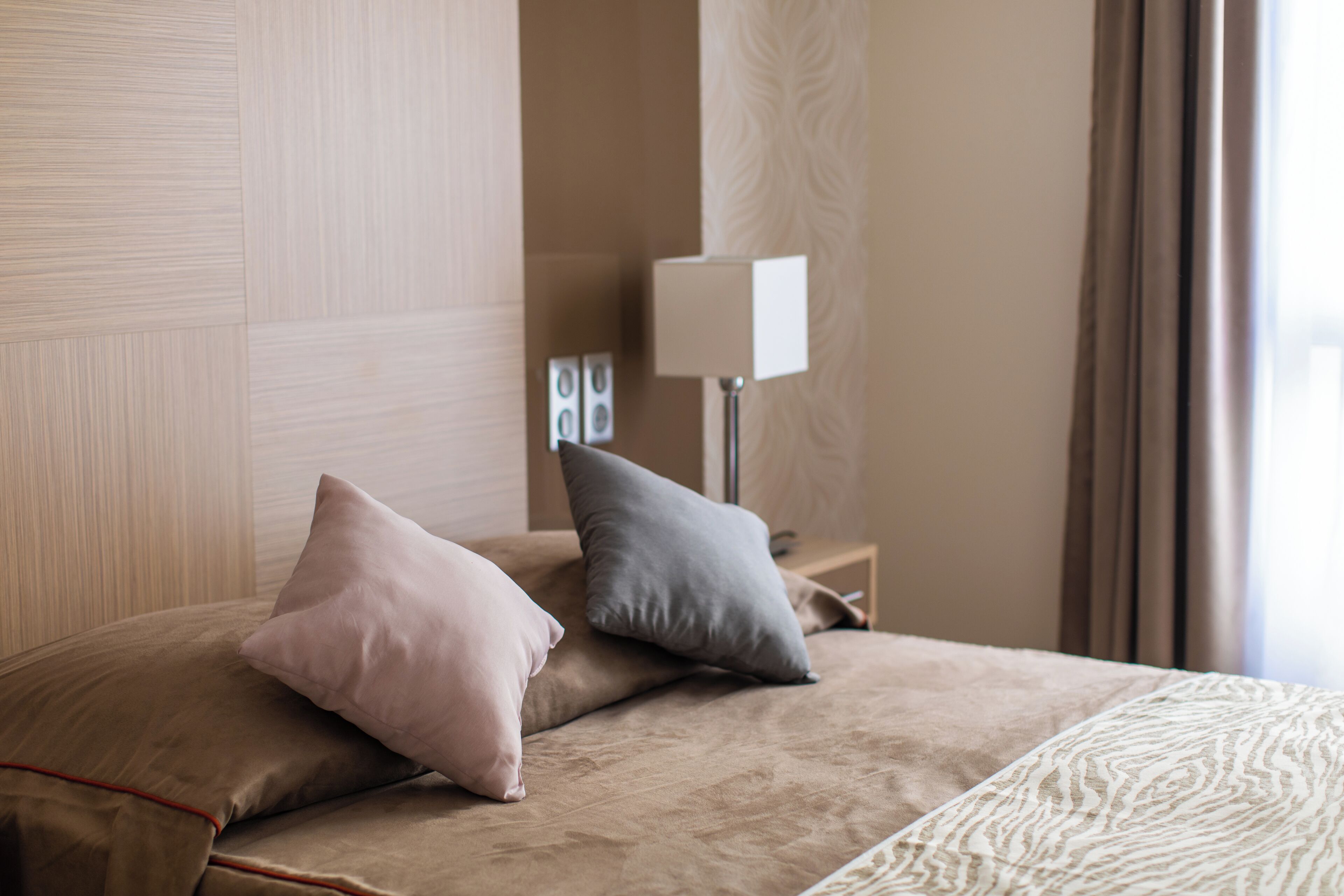 A neatly made bed with two pillows, a bedside lamp, and a patterned rug.