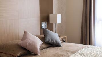 A neatly made bed with two pillows, a bedside lamp, and a patterned rug.