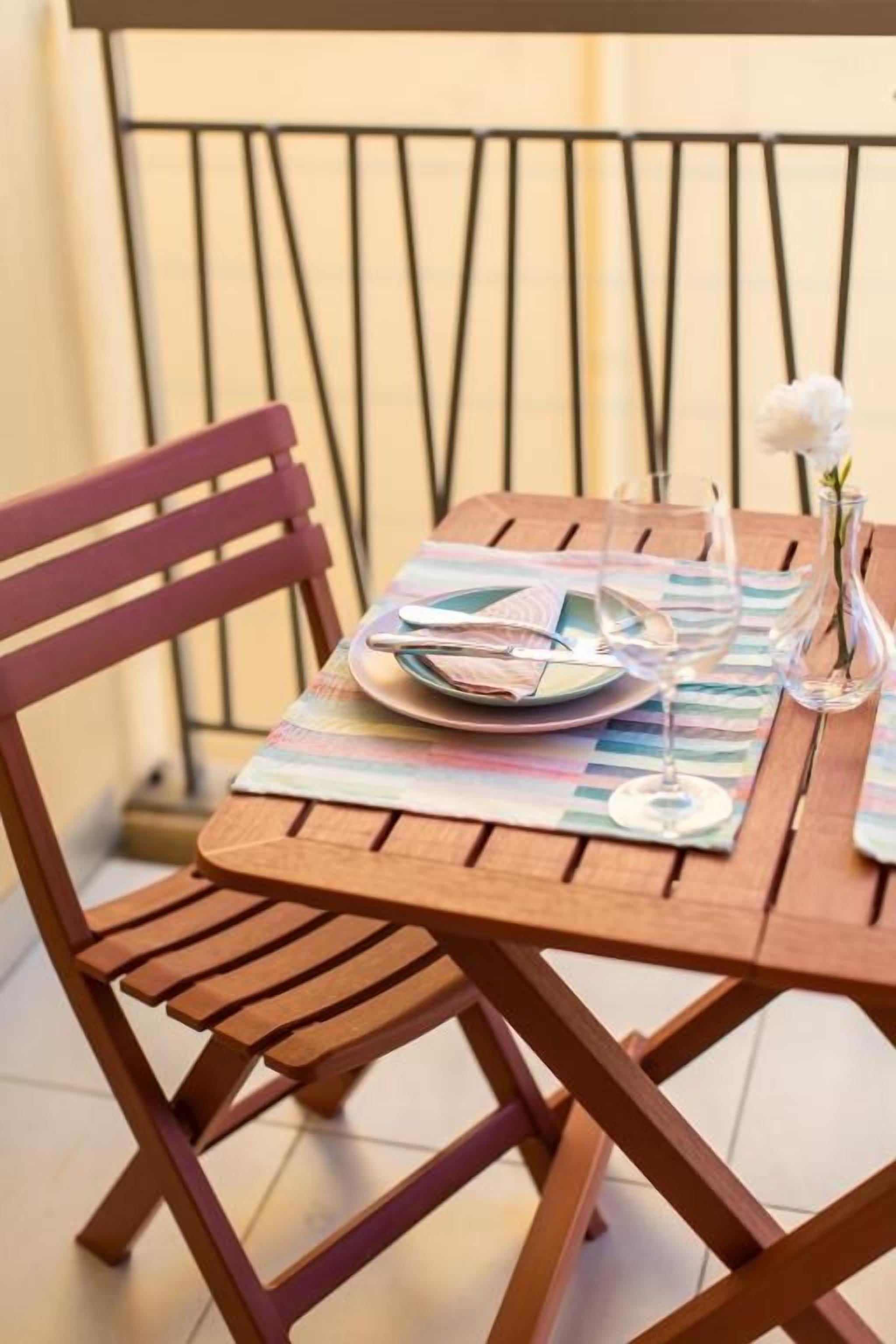 A wooden table with a placemat, a plate, a glass, and a vase with a single flower.