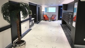 Un vestíbulo de hotel con piso de mármol, un mostrador de recepción, una planta grande en maceta, dos sillas y una caja fuerte empotrada en la pared.
