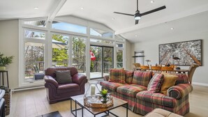 Un salon spacieux avec une grande fenêtre, un ventilateur de plafond et un canapé à motifs écossais.