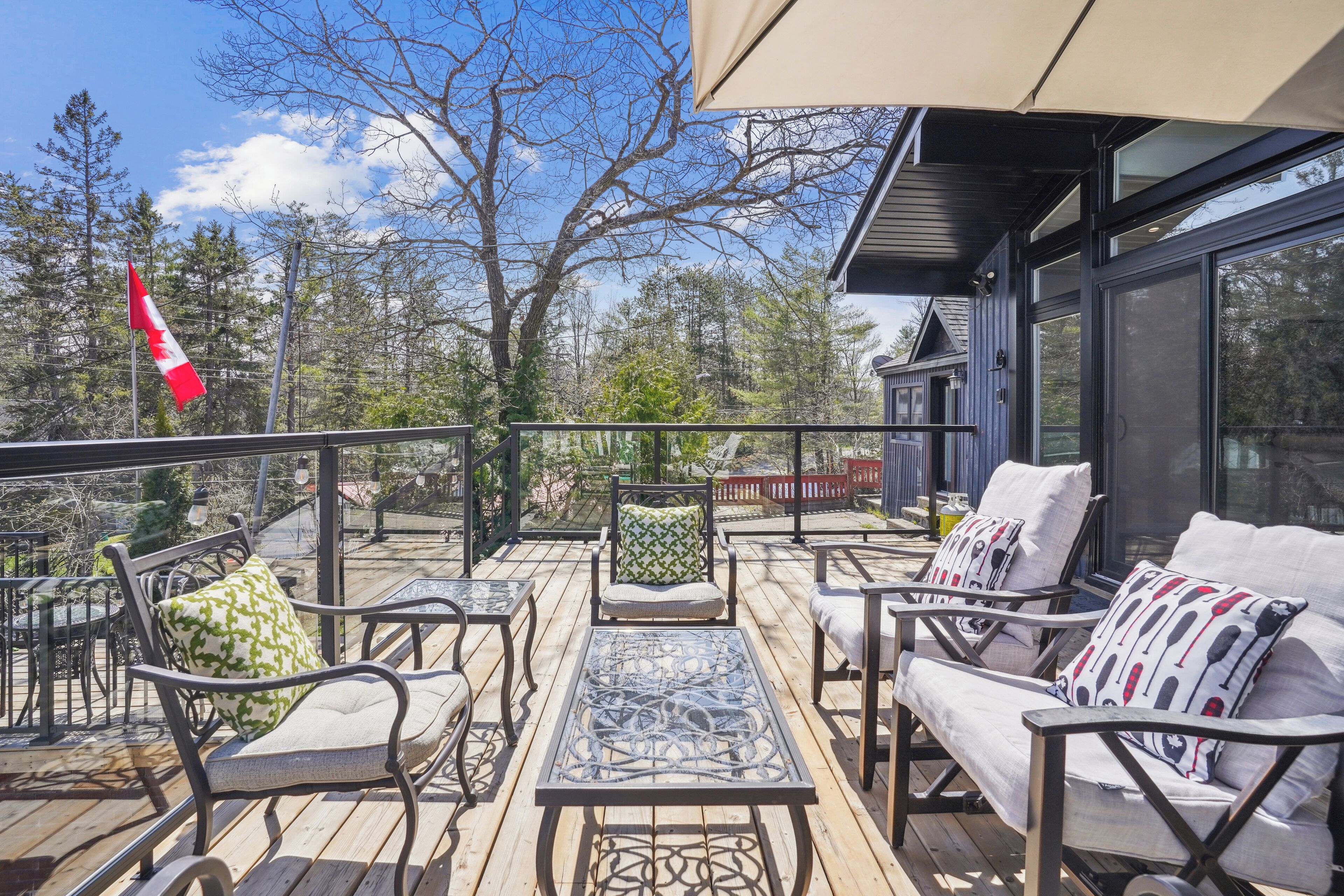 A deck with outdoor furniture, a flag, and a view of trees and a building.