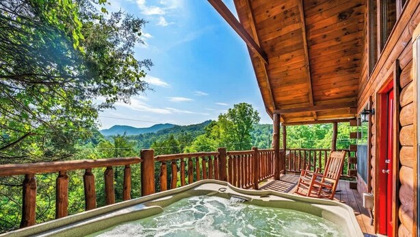 Une terrasse en bois avec un jacuzzi et des chaises, offrant une vue sur un paysage boisé.