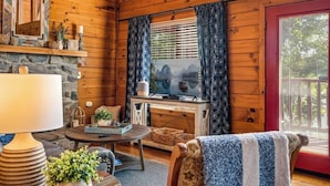 L’intérieur chaleureux d’un chalet avec une cheminée en pierre, un téléviseur et un coin salon confortable.