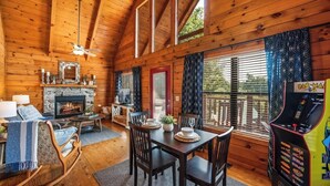 Un intérieur de chalet chaleureux avec une cheminée, des murs en bois, un coin repas et une borne d’arcade Pac-Man.