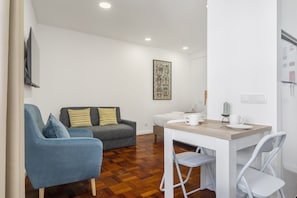 Un espace de vie compact comprenant un canapé, une table à manger avec des chaises, un téléviseur à écran plat fixé au mur et un élément décoratif mural.