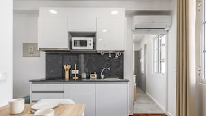 A modern kitchen with white cabinets, a microwave, and a sink. There is a wooden table with plates and cups. - Ribeira do Esmeraldo 3B by Madeira Sun Travel (Funchal)