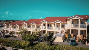 A row of two-story motel buildings with balconies, a parking area, and a clear blue sky. - Venetian Breeze Cozy Studio #7 (Venetian Road Settlement)