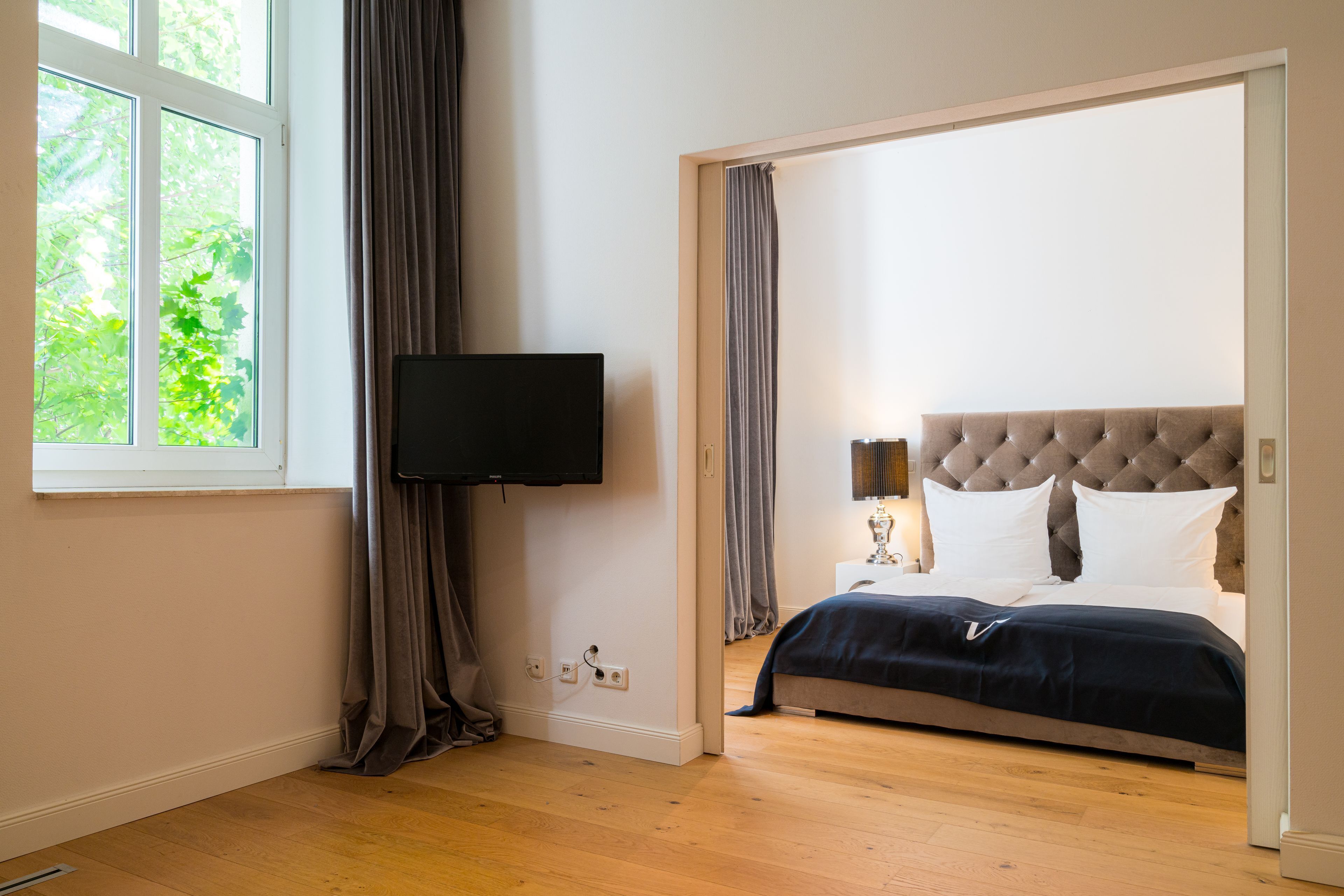 Une chambre à coucher avec un lit, un téléviseur fixé au mur et une fenêtre avec des rideaux.