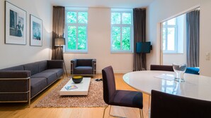 A modern living room with a sofa, armchairs, a coffee table, and a dining table. There are two windows with curtains, a flat-screen TV, and framed pictures on the wall. - Vienna Residence Frankfurt, Schweizer Platz #6074 (Frankfurt)