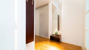 Un pasillo con suelo de madera en patrón de espiga, una puerta de madera oscura y una pequeña planta sobre una consola de madera.