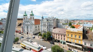 Eine Stadtansicht mit historischen Gebäuden, einer markanten Kirche mit grünen Kuppeln sowie einer Straße mit Geschäften und Fahrzeugen.