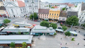 Ein Stadtplatz mit einem großen Gebäude, einer Straßenbahnhaltestelle und verschiedenen Geschäften.