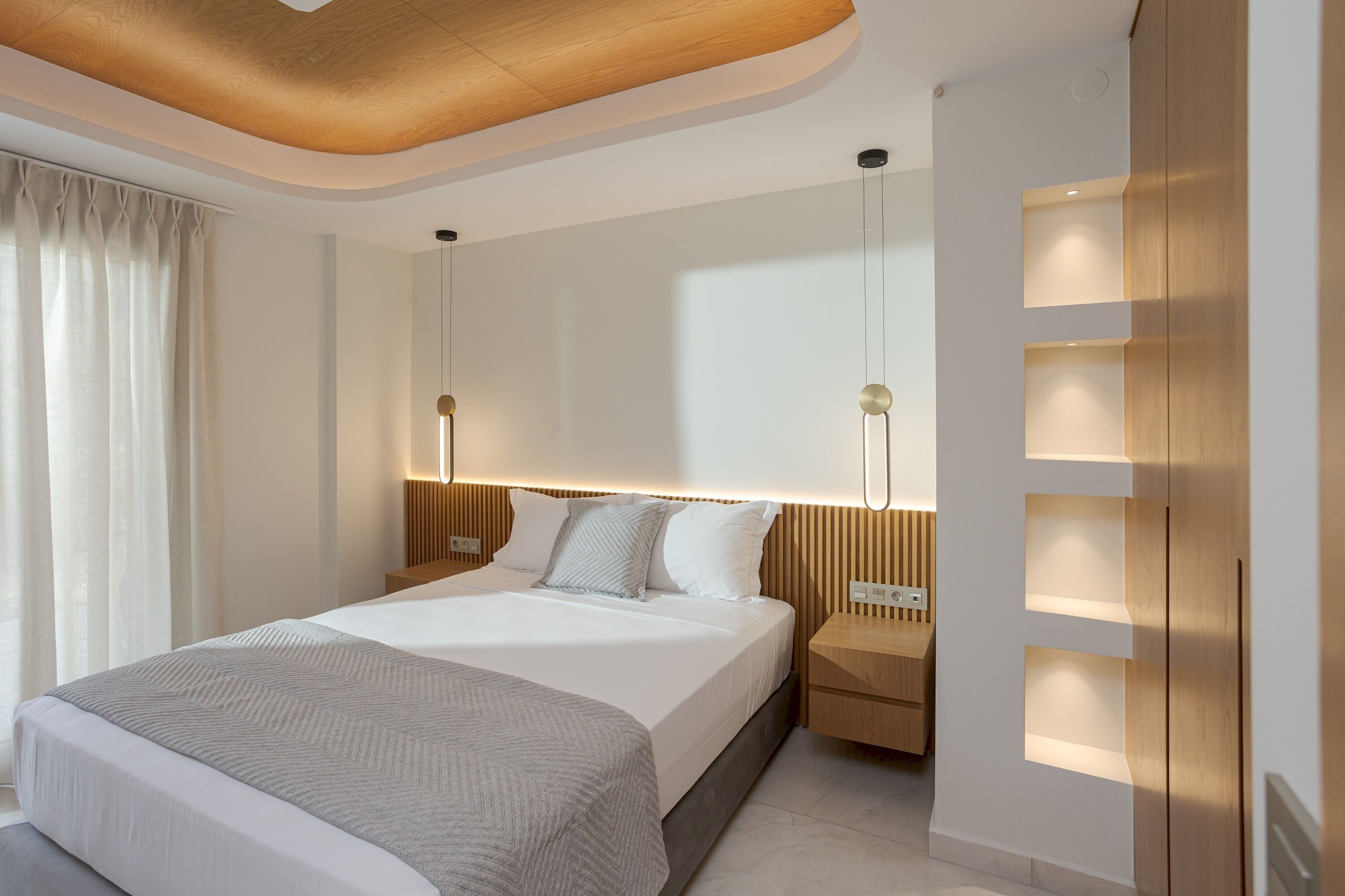 A modern hotel room with a large bed, bedside tables, and built-in lighting.