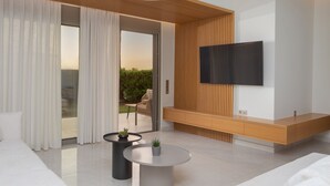 A modern living room with a large TV, a sofa, a coffee table, and a sliding glass door leading to a balcony. - Adore Gold Natural Retreat by Estia (Perama)