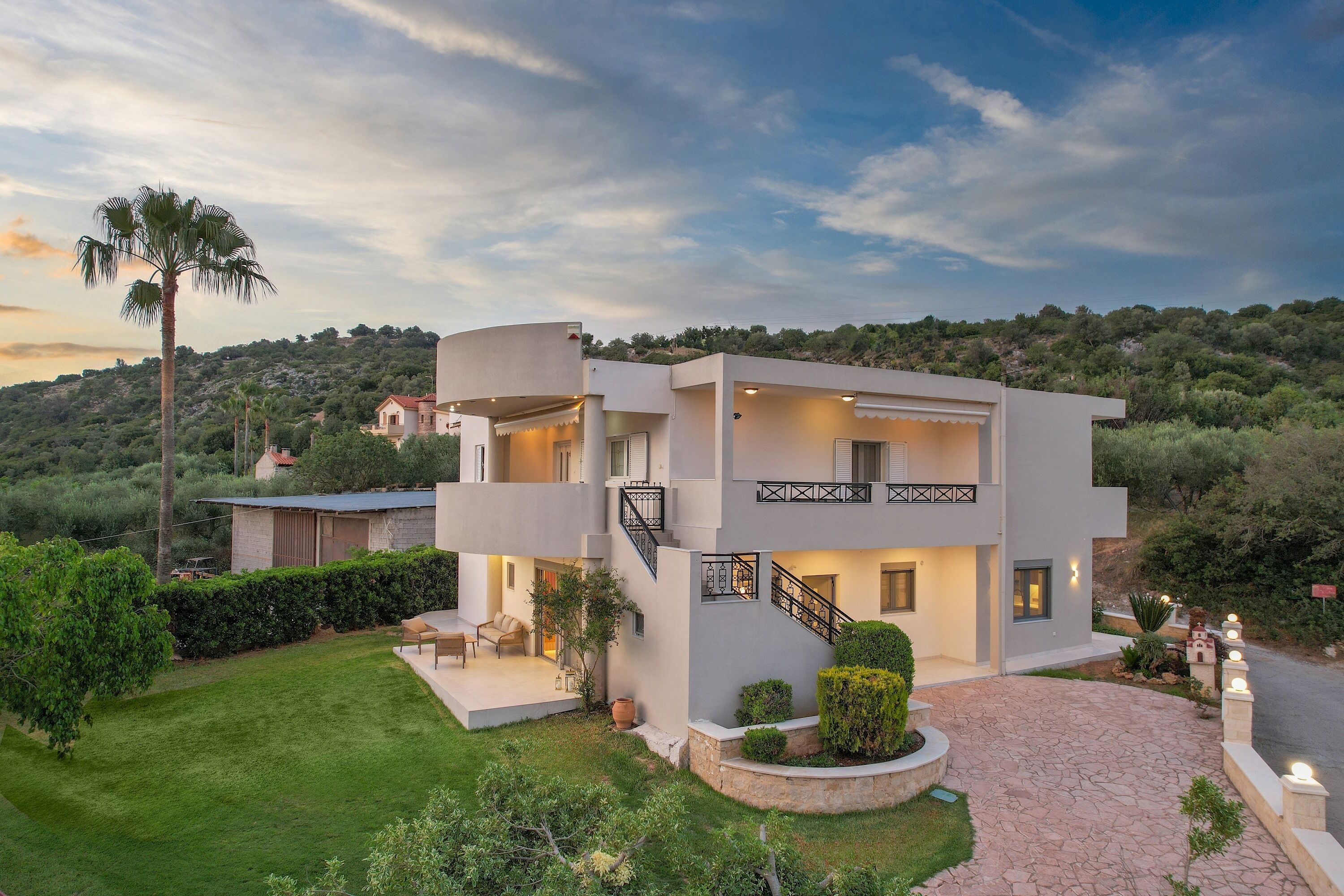 Une maison moderne à deux étages, dotée d’un jardin aménagé, d’une terrasse et d’un escalier menant à l’étage supérieur.