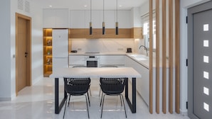 A modern kitchen with white cabinetry, a central island, black chairs, and pendant lights. - Adore Gold Natural Retreat by Estia (Perama)