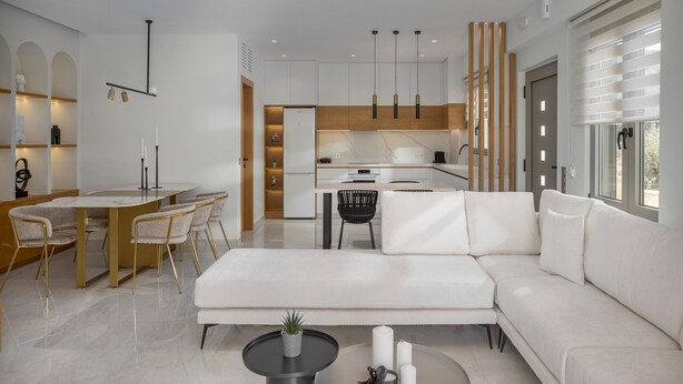 A modern living room with a white sofa, a dining area with a round table and chairs, and a kitchen in the background. - Adore Gold Natural Retreat by Estia (Perama)