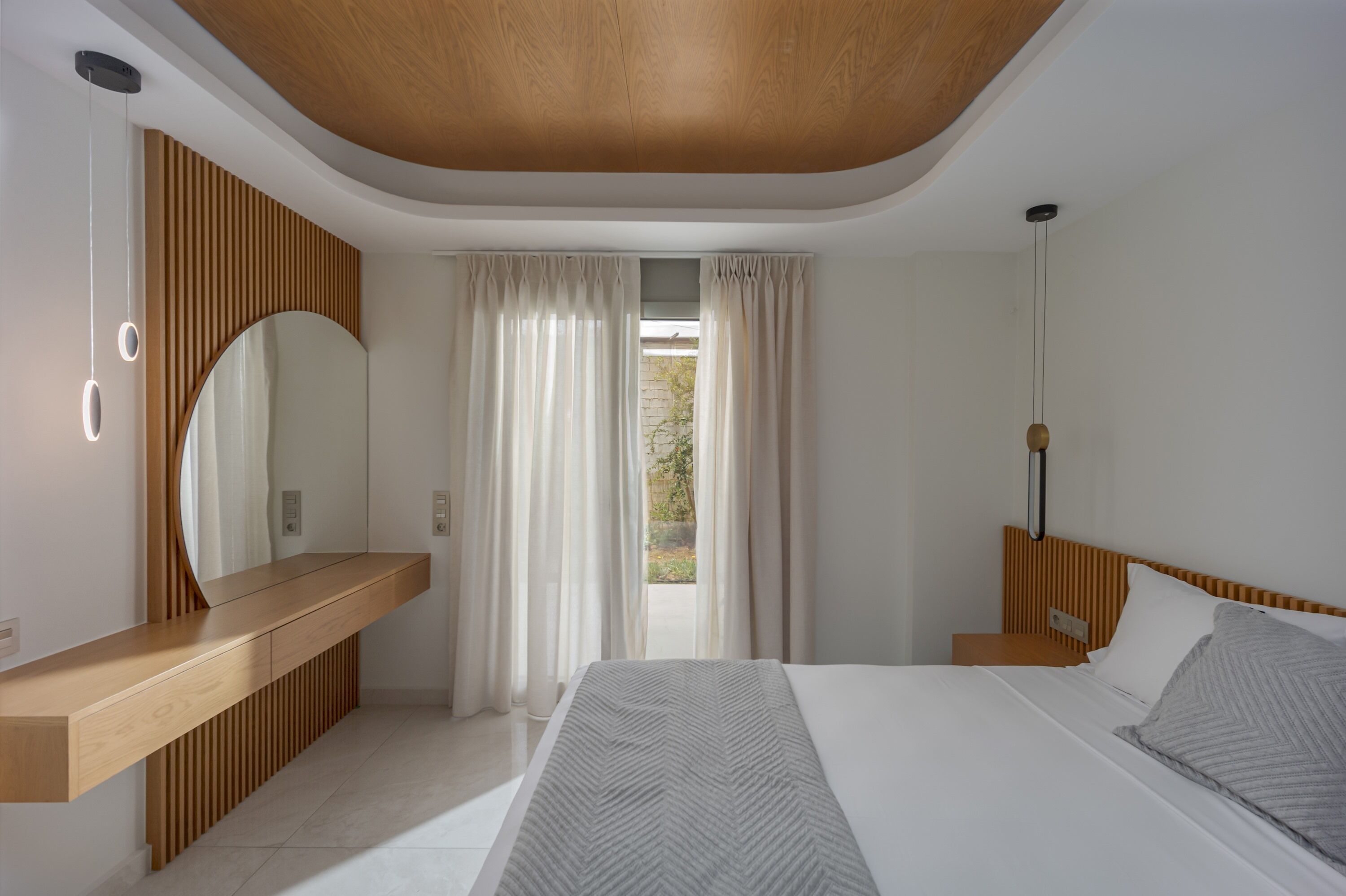 Une chambre moderne avec un plafond en bois, un grand lit, une table de chevet, un miroir et une vue sur l’extérieur.
