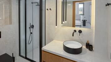 A modern bathroom with a glass-enclosed shower, a round sink, and a mirror above the vanity.
