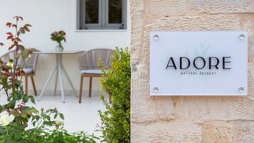 A sign for 'ADORE Natural Retreat' mounted on a stone wall.