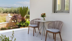 Un patio con dos sillas de mimbre, una mesa, un florero con flores y vistas al paisaje.