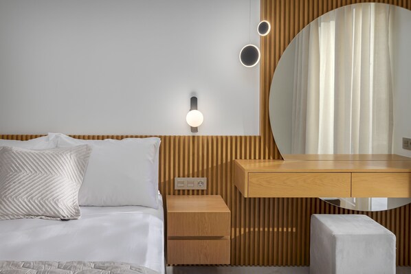 A modern bedroom with a wooden headboard, a bedside table with a lamp, a round mirror, and a white bed with patterned pillows. - Adore White Natural Retreat by Estia (Perama)
