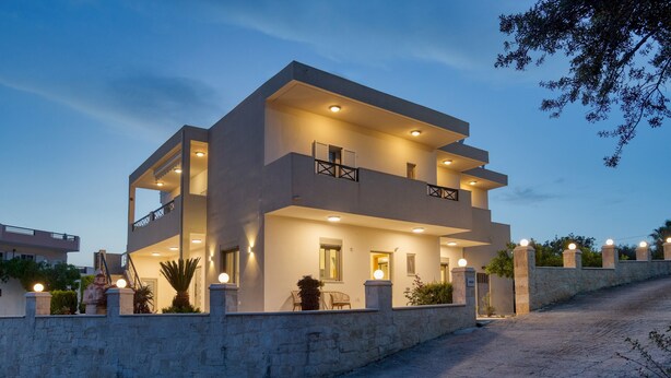 Una casa moderna de dos pisos con muro de piedra, varios balcones e iluminación exterior.