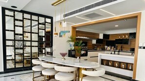 A modern kitchen with a central island, a dining area with a round table and bar stools, and a decorative mirror wall. - Nile view appt, Cornish al Nile (Cairo)